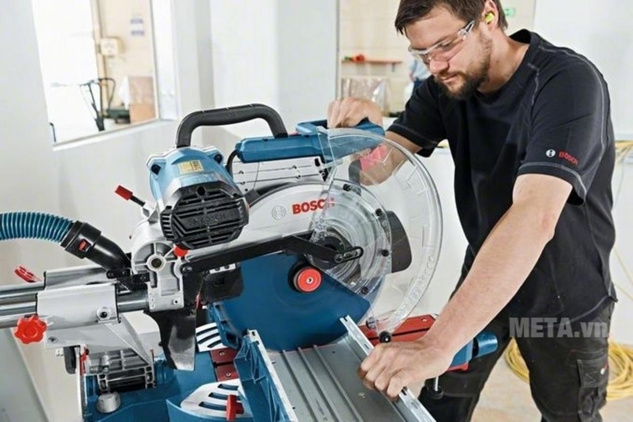Công suất mạnh mẽ và lưỡi 305 mm hỗ trợ cắt vật liệu lớn hiệu quả (Bosch GCM 12 SDE). Ảnh mẫu cắt gỗ dày và thanh nhôm lớn trong xưởng nội thất Việt Nam - high-res, workshop setting, action shot, shallow depth of field, natural light, color accurate, no clutter, realistic).