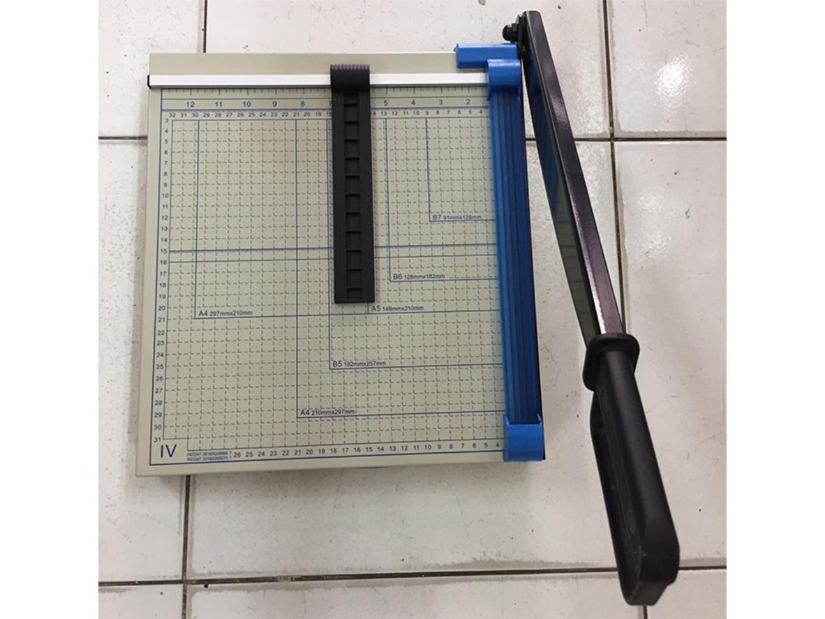 Close-up lưỡi dao thép và phần gá lưỡi của Bosser GD-04 A4 (show wear-resistant blade). The image should show metal texture and safety guard visible for trust cues and clarity of mechanism (close-up). The background is a clean office desk with A4 paper stack nearby for scale.