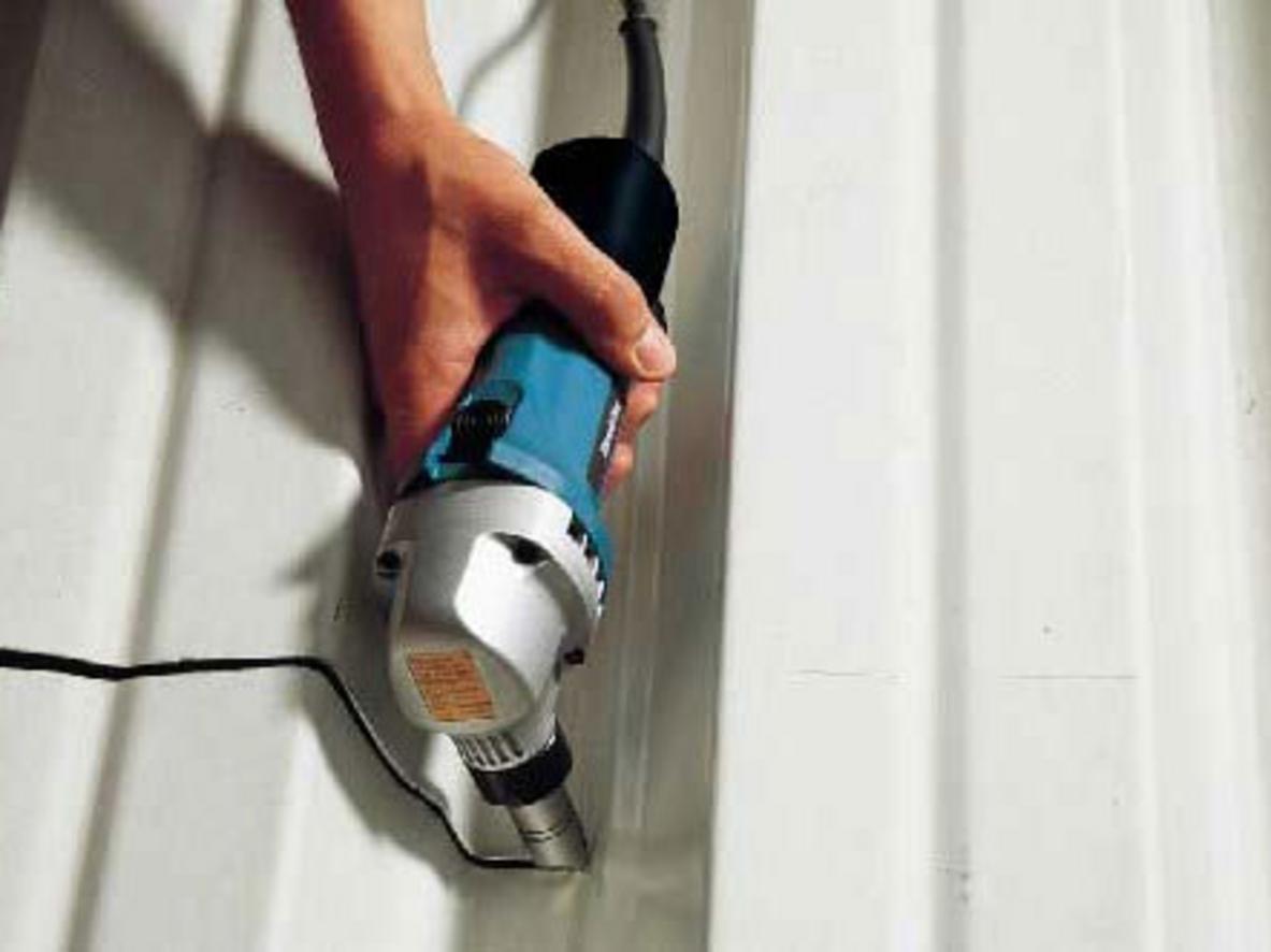 Người thợ cầm máy Makita JN1601 trên mái tôn, thể hiện tư thế làm việc thoải mái và kích thước nhỏ gọn; wide shot; natural lighting; high detail.