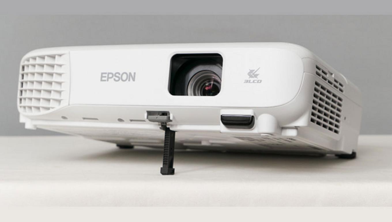Cổng HDMI/VGA/USB-B và thiết kế di động; imagePrompt: Photo showing the projector ports and a person carrying the compact projector.